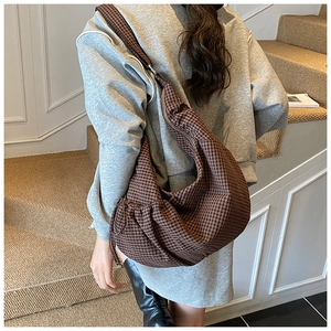 Detail of a large brown plaid hobo bag worn crossbody against a retro wall backdrop