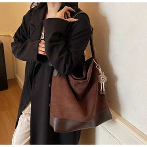 Detail of a brown suede patchwork tote bag with a plush charm and leather straps