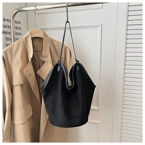 Close-up of black matte suede tote bag hanging on a rack against a stylish trench coat