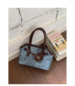 Detailed view of blue canvas handbag featuring brown leather trim and silver horsebit buckle