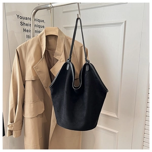 Close-up of black matte bucket bag hanging with khaki trench coat in soft light