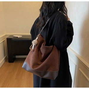 Close-up of brown suede tote bag featuring leather patchwork and a white plush charm