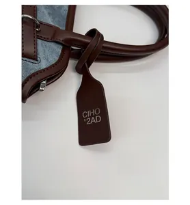Close-up of brown leather handle, metal ring, and CIHO brand tag on denim handbag