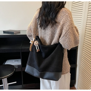 Detail of black patchwork tote bag with suede texture and plush keychain on model shoulder