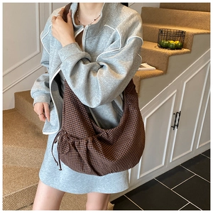 Detail of a brown plaid crossbody bag featuring drawstring side pleats on model