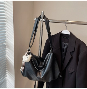 Détail du sac hobo en cuir noir avec chaîne métallique et breloque ours en peluche