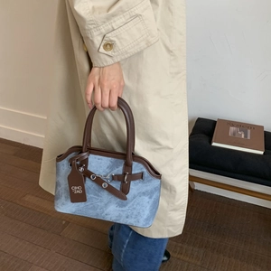 Detail of vintage blue suede handbag with brown leather trim held by a woman in a trench coat