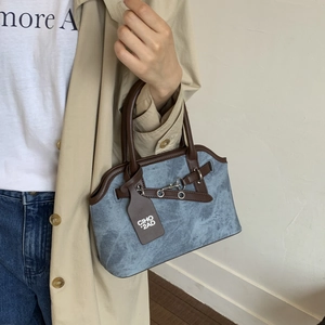 Detail of light blue textured handbag with brown leather handles and metallic buckle