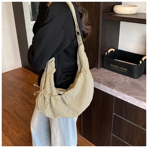 Detail of checkered hobo bag with side bow tie strap, shown worn by a model in a room