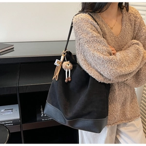 Detailed side view of large black tote bag with leather base and plush pendant