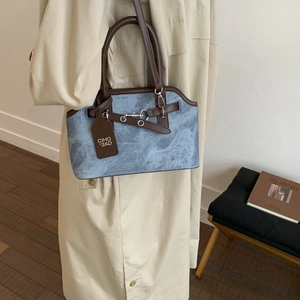 Close-up of blue matte textured handbag with brown leather handles and metal buckle detail