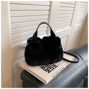 Détail du sac seau noir en fausse fourrure avec poignées en cuir sur des livres blancs