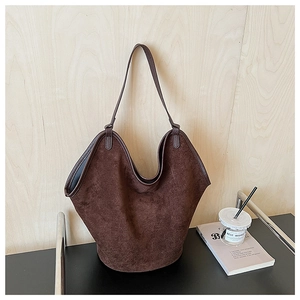 Detail view of large brown suede tote bag with extendable wing design on a dark surface