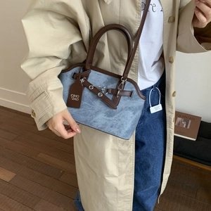 Close-up of blue textured crossbody bag with brown leather handles and metallic buckle
