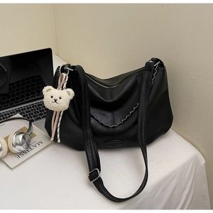 Détail du sac en cuir souple noir avec chaîne argentée et adorable porte-clé ours blanc