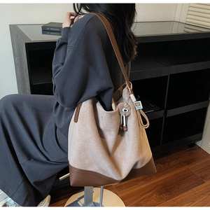Detail of a large beige suede tote bag with brown leather accents and a plush charm