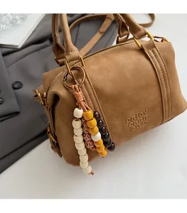 Detail of a brown cylindrical pillow bag with bohemian beads and golden hardware accents