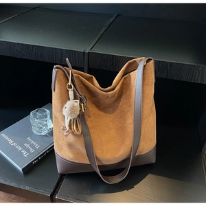 Detail of a brown suede hobo bag with leather base and plush pendant on wood