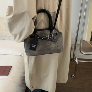 Detail view of grey frosted handbag with black trim, metal grommets and brand tag