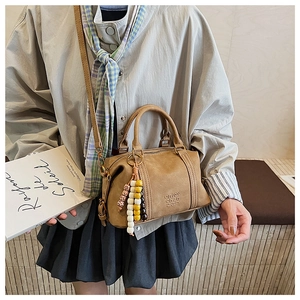 Detail of camel crossbody pillow bag with beaded charm and embossed logo detail