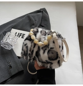 Detail der Leoparden-Kunstpelltasche mit Perlengriff und weißem Riemen auf grauem Stoff