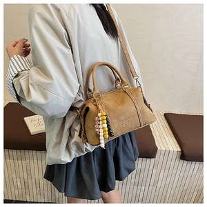 Close-up of tan matte crossbody bag with beaded pendant worn by a model in casual outfit