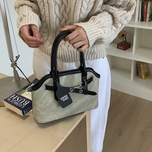 Detail of sage green suede handbag with black leather handles and metallic buckle hardware