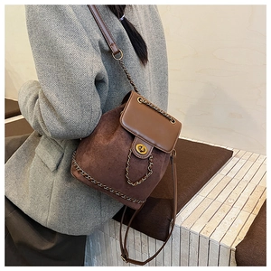 Detail of a dark brown suede and leather bucket bag featuring gold chain and twist lock