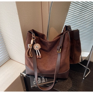 Detail of dark brown suede tote bag with plush charm in a warm aesthetic indoor setting