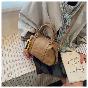 Detail of vintage brown cylinder bag with embossed letters and colorful ball charms