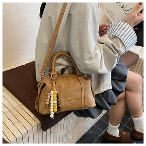 Detail of a vintage brown boston bag featuring a matte texture and rainbow bead charm