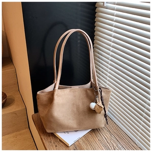 Detalle de bolso tote de ante marrón con correas finas y colgante de béisbol