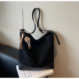 Detail of black suede hobo bag with smooth leather trim and decorative plush keychain charm