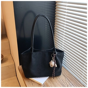 Detalle del bolso tote de ante negro con colgante de béisbol sobre mesa de madera rústica