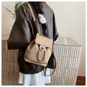 Rear view of model wearing a khaki canvas backpack with tan leather details and chain strap