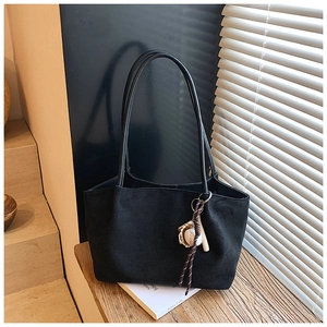 Detalle de bolso tote de ante negro con llavero de béisbol sobre superficie de madera