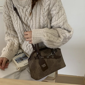 Close-up of brown vintage crossbody bag with CIHO'2AD tag on soft beige knit sweater