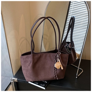 Detalle del bolso tote de ante marrón oscuro con correas finas y colgante decorativo
