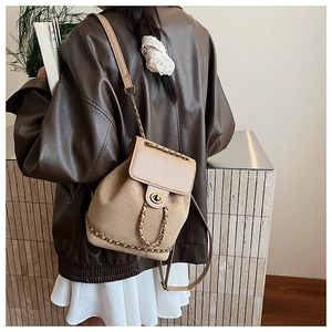 Detailed view of dual-texture backpack with beige leather flap and gold chain lock
