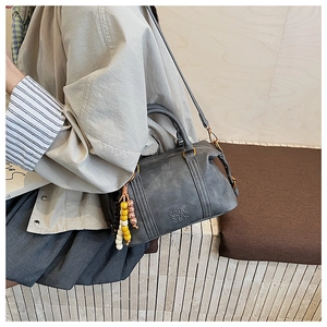 Detail of grey retro Boston bag with vintage leather texture and beaded pendant