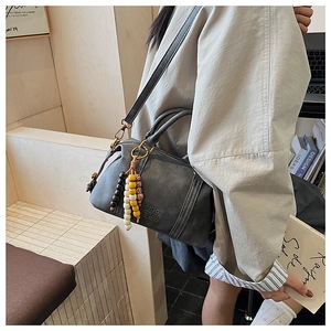 Detail of dark grey retro Boston bag with beaded charm and adjustable strap worn by model