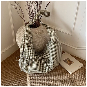 Detail of green plaid crescent bag featuring adjustable strap and side bow decoration