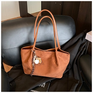 Detalle de bolso tote de ante marrón con colgante de béisbol en silla de cuero negro
