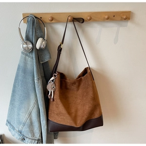 Detail of a large brown suede tote bag featuring contrast leather base and plush pendant