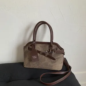 Macro detail of brown suede crossbody bag with vintage buckle and brand hangtag