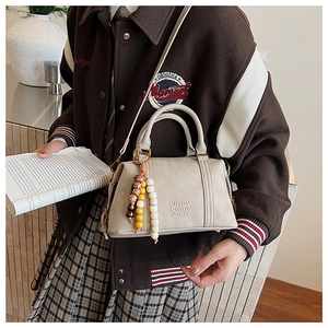Close-up of cream Boston bag with leather letter embossing and vintage beaded charm