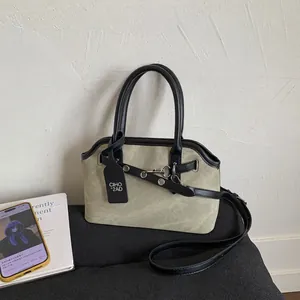Detail of beige canvas tote with black leather trim, metal buckle, and detachable strap
