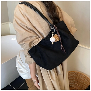 Detalle de bolso tote de ante negro con colgante de béisbol y accesorio de cuerda trenzada