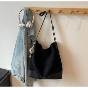 Detail of minimalist black suede tote bag with plush charm on a wooden wall hook
