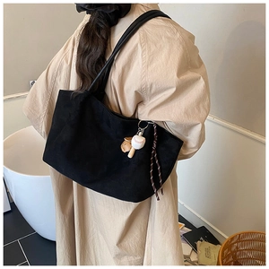 Detalle del bolso tote de ante negro con correas de cuero y colgante de béisbol